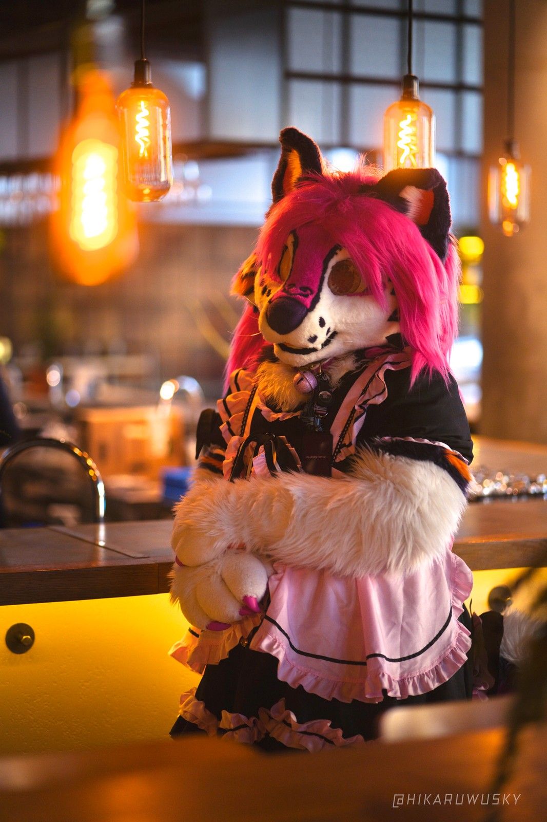 Peechy in a pink maid dress in a café with warm hanging lamps